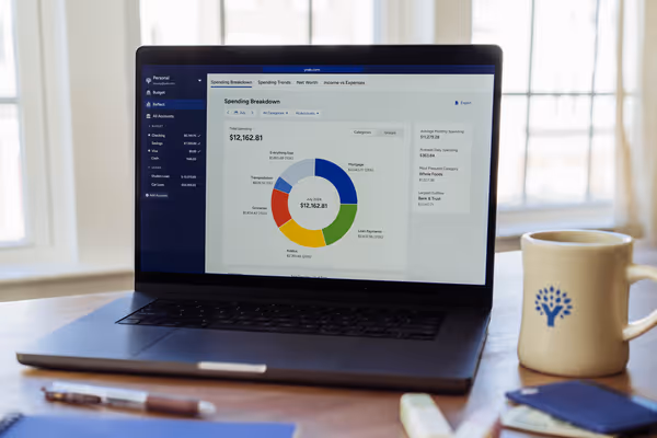 A laptop computer on a desk shows the YNAB web app open to a spending breakdown report.